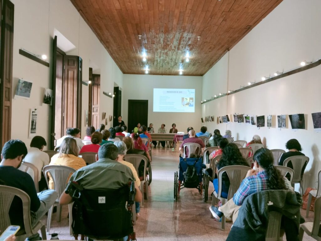 Fotografía vista dede el fondo hacia el frente del salon con las personas que nos mientras se desarrolla el conversatorio