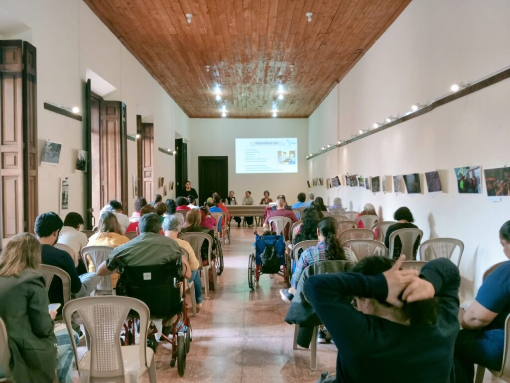 Fotografía vista dede el fondo hacia el frente del salon con las personas que nos mientras se desarrolla el conversatorio